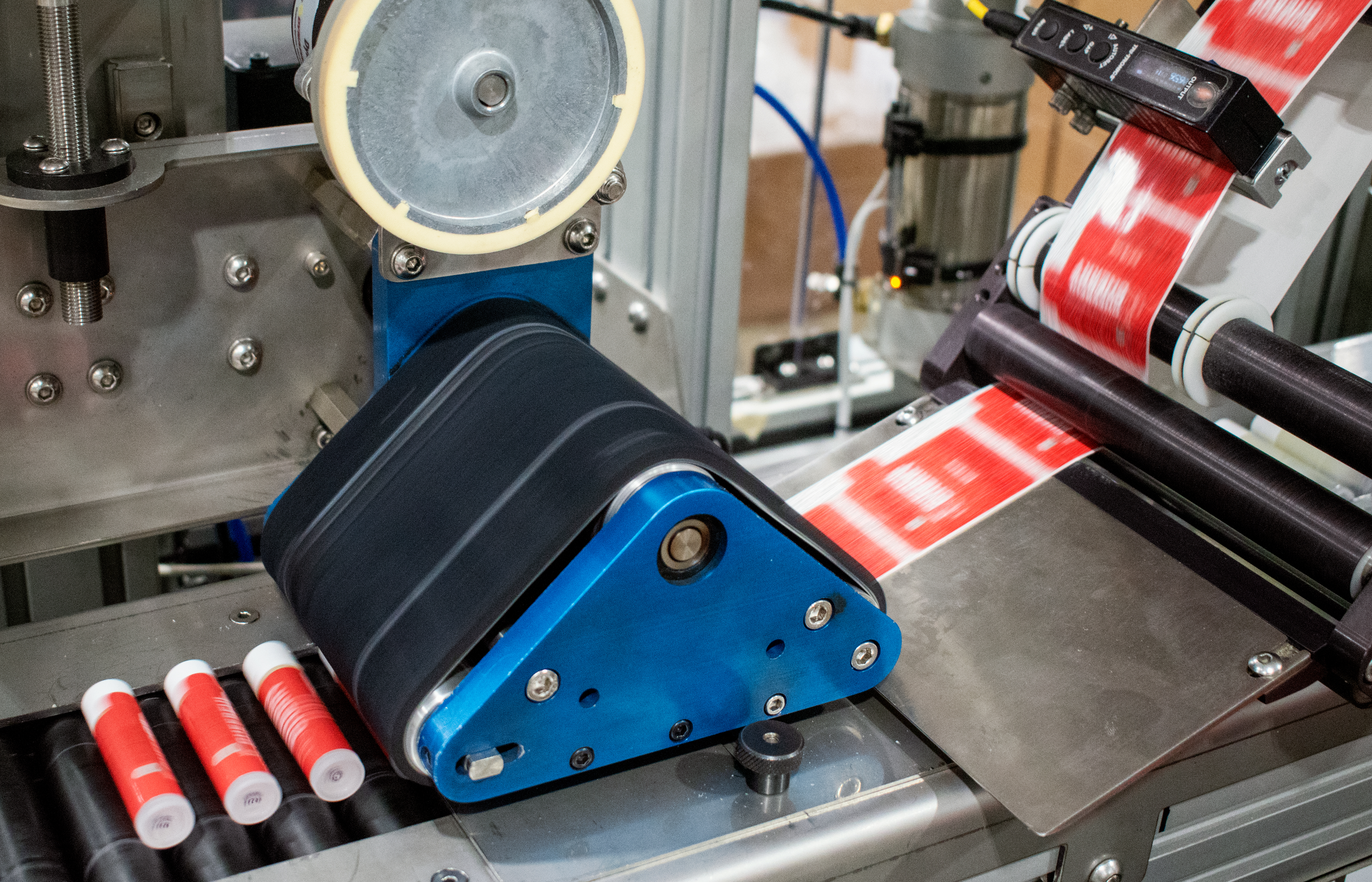 A labeling machine wraps white lip balm tubes in Eco Lips' red label.