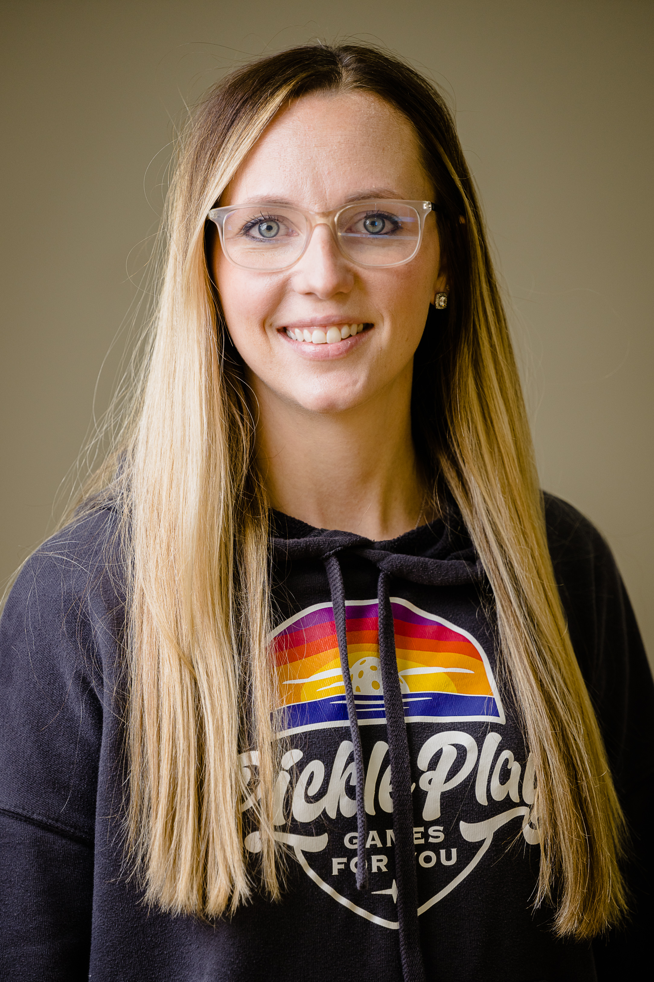 Blake Renaud, blonde hair and glasses, smiles at the camera wearing a branded PicklePlay sweatshirt.