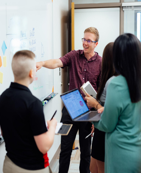 A group of people work together using laptops and a whiteboard