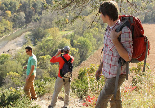 Three young men hiking in Iowa look down over a flowing river